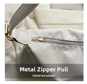 Detail of high-quality gold hardware zipper on white minimalist nylon shoulder bag