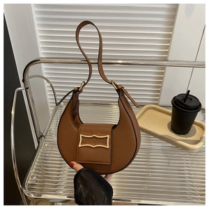 Détail du sac selle marron en demi-lune avec boucle dorée dans un décor de style de vie