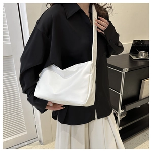 Close-up of white crossbody bag with wide shoulder strap against a black shirt