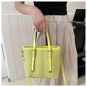 Detail view of woven yellow-green bucket bag with stylish vertical texture and gold buckles