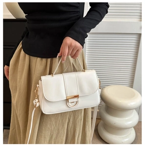 Close-up of white crossbody bag with gold semi-circle clasp and adjustable shoulder strap