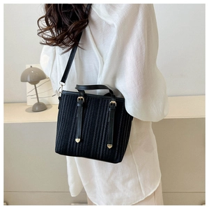 Detail of a black striped bucket bag with gold buckles worn over the shoulder by a model