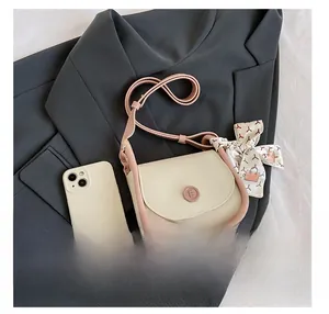Detail of a beige and pink saddle bag with decorative scarf next to a mobile phone