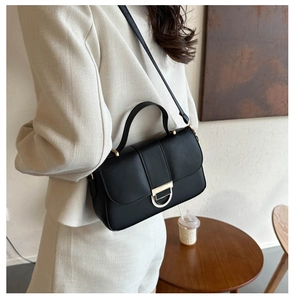 Detail of a chic black leather handbag featuring a prominent D-shaped gold metal buckle