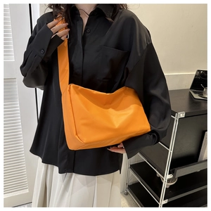 Model wearing a minimalist bright orange crossbody bag with wide shoulder strap details