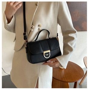 Fashionable black leather handbag with a unique semicircular metal clasp and adjustable strap