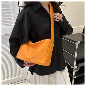 Side view of a bright orange crossbody bag with wide strap on a model wearing black shirt