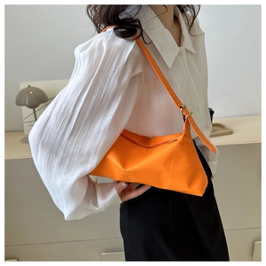 Vibrant orange shoulder bag shown on model with minimalist rectangular leather silhouette