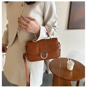 Detail of a brown leather shoulder bag featuring a silver D-ring magnetic clasp closure