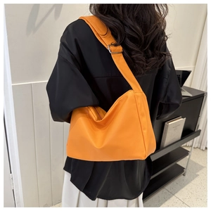 Bright orange crescent shoulder bag with wide strap worn with a minimalist casual outfit