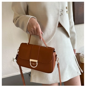 Detail of caramel leather handbag featuring golden D-buckle and elegant top handle