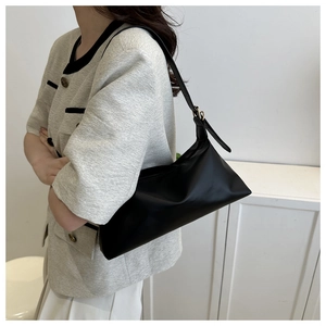 Minimalist black matte PU leather shoulder bag styled on model with beige jacket