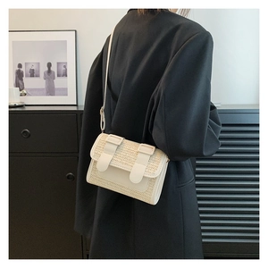 Detail of straw woven crossbody bag with PU leather flap shown on a black suit jacket
