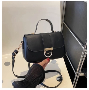 Detail of black crossbody square bag featuring textured leather and gold metal ring clasp