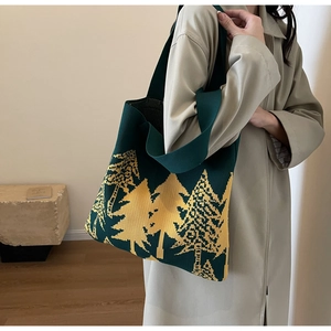 Detail of dark green knitted tote bag featuring a yellow pine tree pattern worn by a model