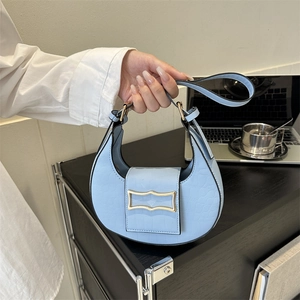 Sac à main croissant bleu clair avec motif crocodile et fermoir doré chic sur marbre