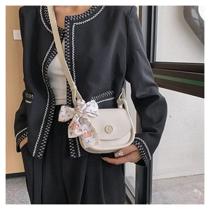 Close-up of a beige mini flap bag with a metal logo and decorative silk scarf bow detail