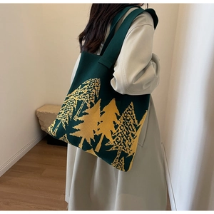 Detail of green knitted tote bag with pine tree pattern worn by a model in interior