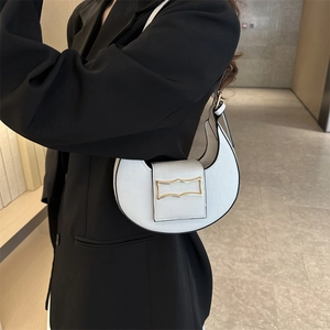 Sac hobo blanc en forme de croissant avec boucle dorée porté sur un blazer noir chic