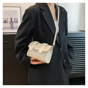 Detailed view of white woven crossbody bag with leather trim on model wearing black suit