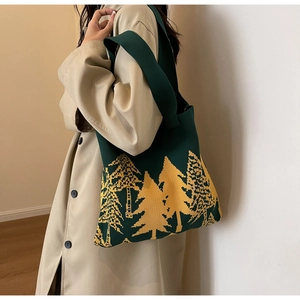 Detail of forest green knitted tote bag with yellow pine tree patterns on a model