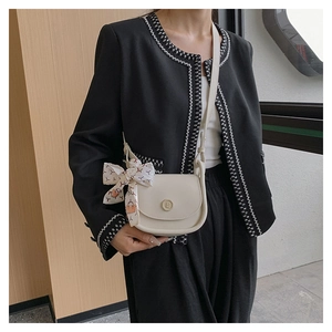Detail of a beige crossbody saddle bag with metal E logo and floral silk ribbon accessory