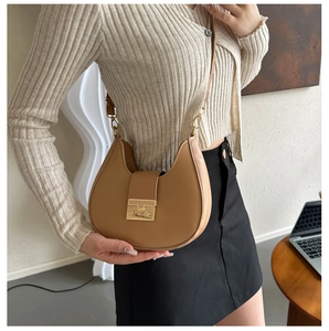 Detail of tan leather saddle bag with gold metal clasp on model in beige cardigan