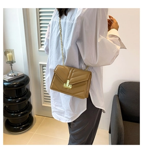 Dettaglio della trama trapuntata a V e catena dorata su una borsa a tracolla color cuoio