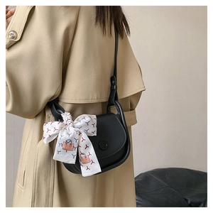 Detail view of a black saddle bag with decorative ribbon scarf on a trench coat