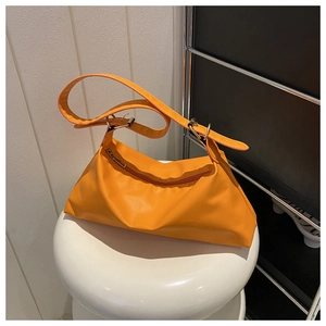 Close-up of bright orange minimalist PU leather handbag with wide strap and silver buckle