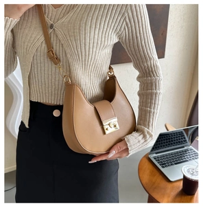 Close-up of khaki leather saddle bag with gold metal lock and adjustable shoulder strap