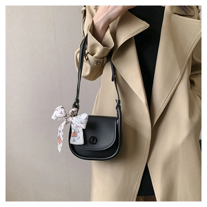 Detail of black leather saddle bag with printed silk scarf on a beige trench coat
