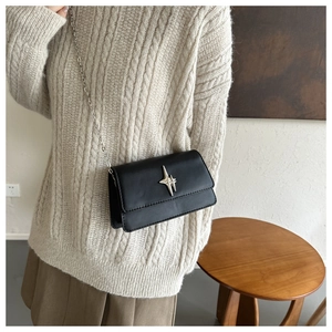 Detail of a black leather crossbody bag with a silver star buckle on a beige sweater background