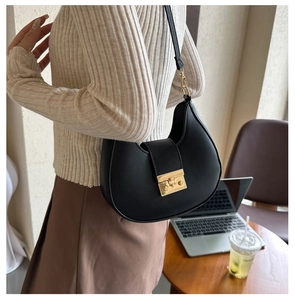 Detail of a black leather saddle bag with a square gold buckle on a model in daily life