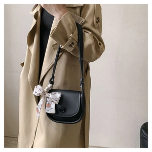 Detail of a black leather saddle bag with printed silk scarf and gold circular buckle