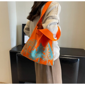 Knitted tote bag with orange and blue mountain landscape pattern shown on a model