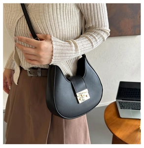 Detail of a black crescent shoulder bag featuring a gold rectangular buckle on soft leather