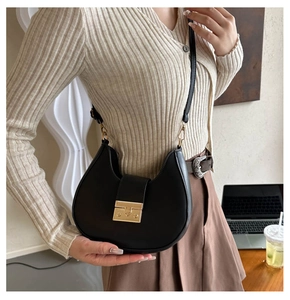 Detail shot of a black crescent shoulder bag with golden lock in a stylish office setting