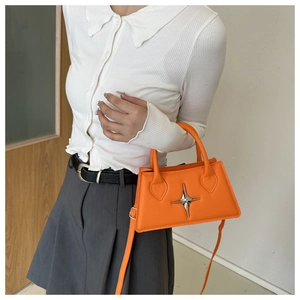 Detail of a bright orange star-adorned crossbody bag on a white shirt and grey skirt model