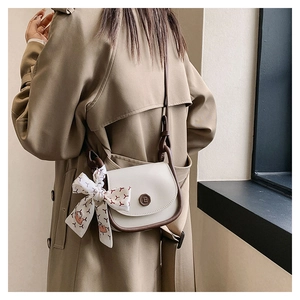 Detail of cream crossbody bag with brown piping and silk ribbon on a trench coat