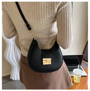 Detail of a black leather saddle bag with gold metal clasp worn over the shoulder