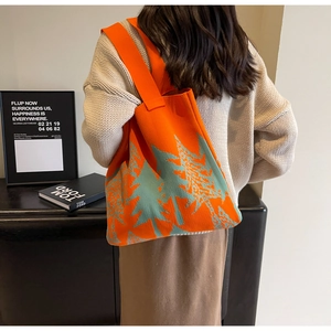 Detail of orange knitted tote bag featuring green tree patterns worn over the shoulder