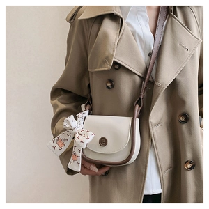 Detail showing vintage cream crossbody bag with contrast brown trim and decorative silk scarf