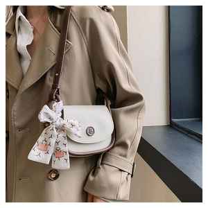 Detail of a cream saddle bag with a decorative silk scarf and leather shoulder strap