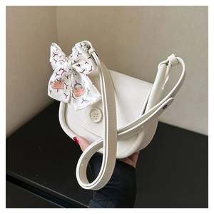 Detail of a beige crossbody bag featuring a golden E-logo and a decorative silk ribbon