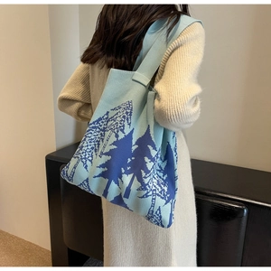 Detail of blue knitted tote bag with tree pattern worn on white dress shoulder