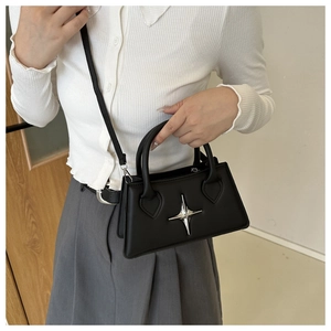 Cross star pendant details on a black leather handbag with crossbody strap shown on model