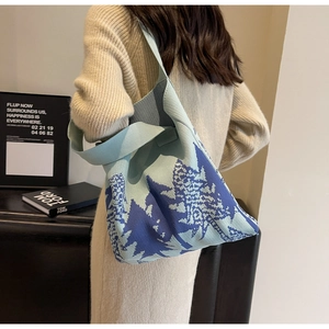 Detail of blue knit tote bag with forest pattern on female model's shoulder
