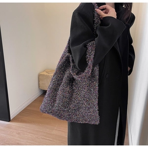 Detailed knit texture of a large tote bag with metallic threads on a black coat