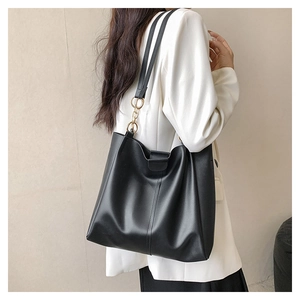 Detail of black matte leather tote bag with gold chain rings on white blazer